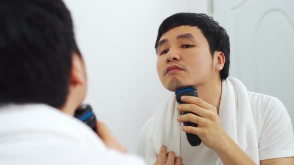 man using electric shave to shaving his face in the bathroom mirror