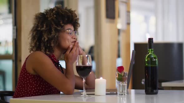 Mixed race woman having a romantic dinner blowing kisses on video chat at home