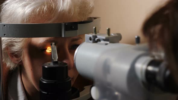 Ophthalmologist Checking Eyesight of Senior Woman with Modern Equipment in Dark Room