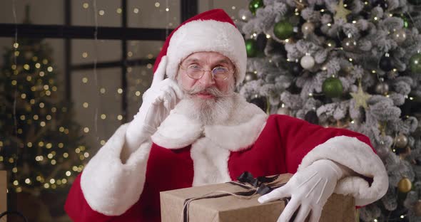 Front View of a Happy Goodnatured Elderly Santa Claus with a Huge Christmas Gift Box Talks By Video
