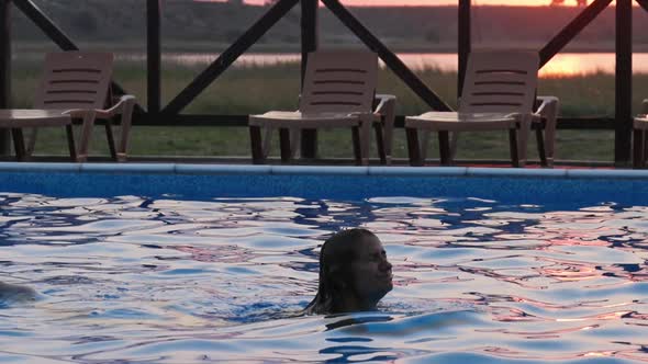 Girl with Wet Hair in Colored Bikini Emerges From Pool with Transparent Clear Water Against