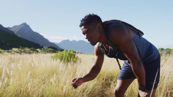 African american man cross country running resting wiping forehead in mountain countryside