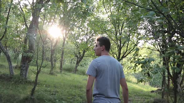 A man walks on a footpath in forest, daytime,  summer season. Young man filmed from behind while Wal