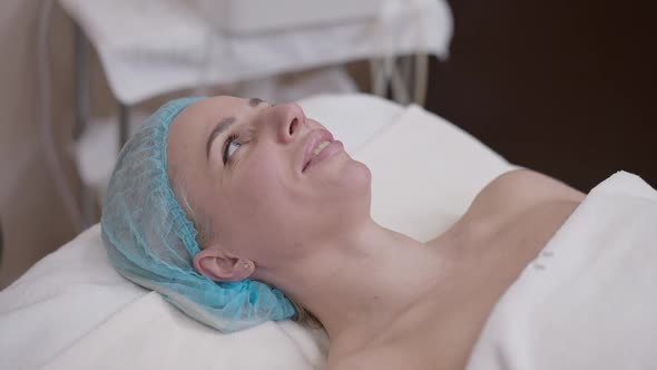 Confident Attractive Caucasian Woman in Shower Hat Lying in Spa Salon Talking Smiling in Slow Motion