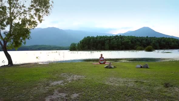 Distant View Girl Changes Yoga Pose on Lake Bank