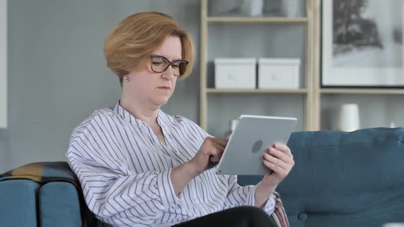 Old Senior Woman Browsing Internet on Tablet PC Sitting on Couch