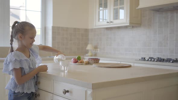 Cute Little Girl Pouring Milk in the Glass in the Kitchen While Her Mother Putting Freshly Baked