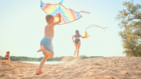 Rear View of Children Running Along Beach in Summer with Kite Flying in Wind