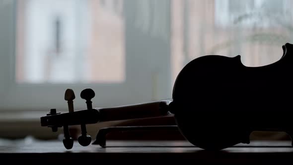 Silhouette of an Antique Violin on a Wooden Table a Bow and a Window in the Background