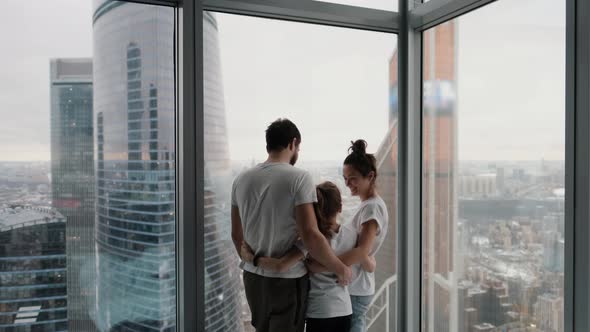 Young Family with Daughter Spending Time Together in Modern Apartment with Large Windows Overlooking