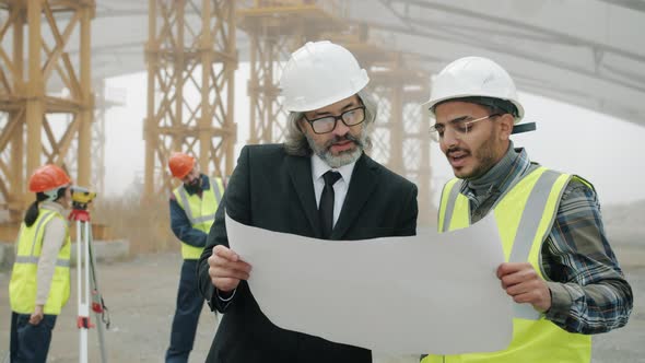 Architect Talking to Engineer in Building Area While Surveyors are Working with Modern Equipment