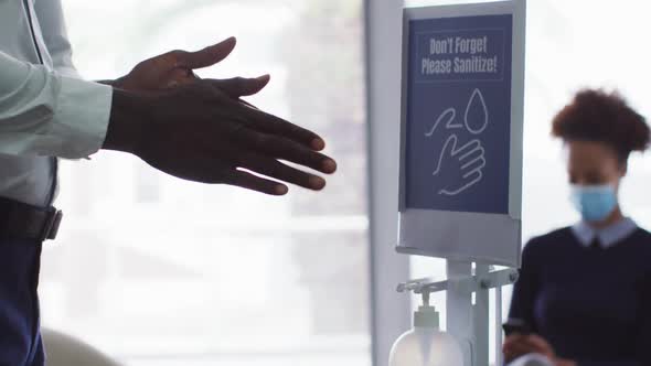 Midsection of african american businessman disinfecting hands upon arrival in office