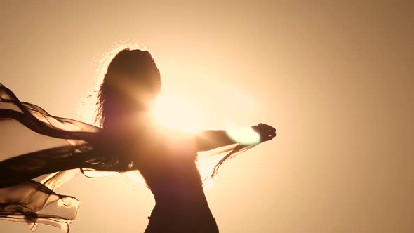 Girl with a Veil in Her Hands Dancing Belly Dance on the Beach. Silhouette