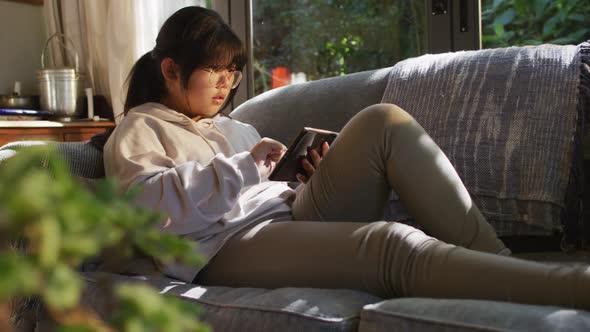 Asian girl lying on couch and using tablet
