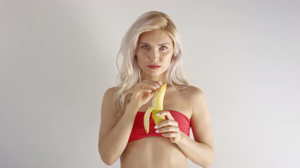 Young Caucasian Blonde in Bikini Top Peeling Banana in Studio