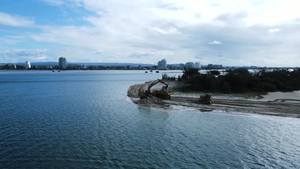 Panning view over water of large machinery working on a sand island creating a new city harbor. High