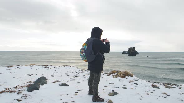 Young Man Tourist Takes Pictures at the Top of the Cliff Around Reynisfjara Beach and Dyrholaey