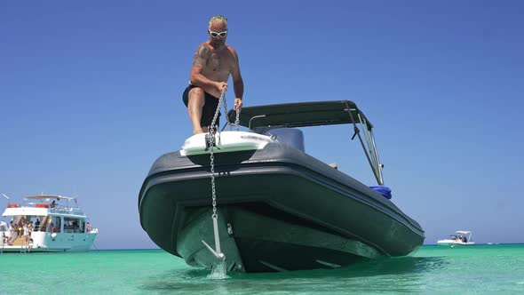 Small Yacht in Turquoise Mediterranean Sea Lagoon with Tattooed Boat Captain Raising Anchor in Slow