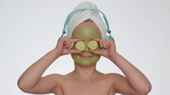 Smiling Child Girl Moisturizing Green Cucumber Mask on Face Listening to Music on Headphones Dancing