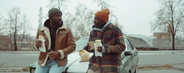 Two African American Men Eating Fast Food and Drinking Coffee by Car