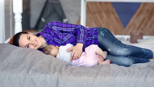 Happy Young Mother Relaxing Hugging Little Baby Sleeping on Bed