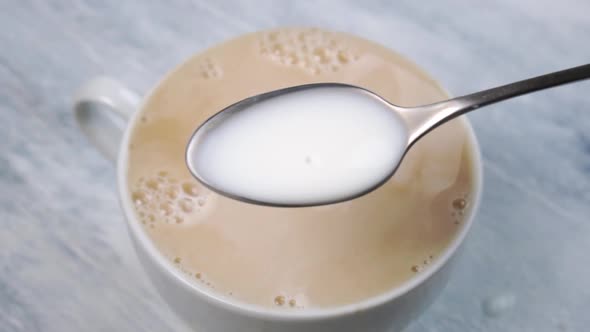 Full teaspoon with milk over white cup with fresh coffee
