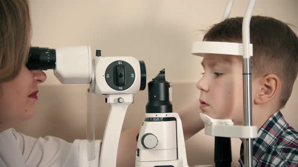 A Little Boy Having a Treatment in Eye Clinic - a Woman Doctor Checking the Eye Vision By Looking