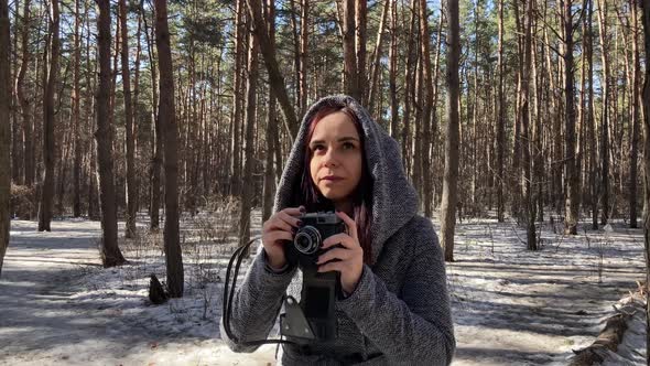 Young Woman in Gray Coat Photographing on Old Photo Camera in Forest