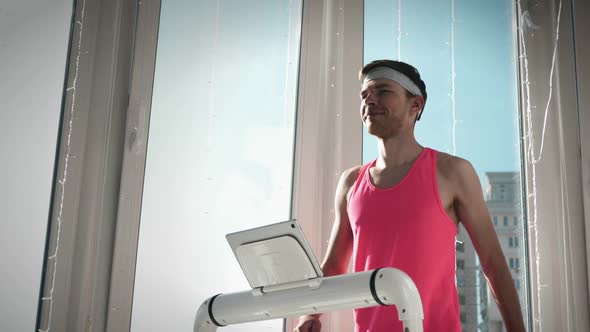 Young funny man in pink outfit is exercising on treadmill 