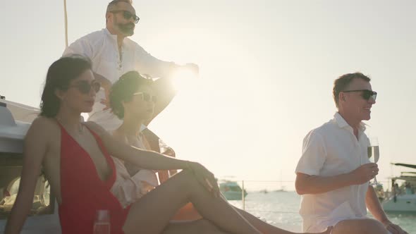 4K Caucasian people drinking champagne while catamaran boat sailing in the sea at summer sunset.