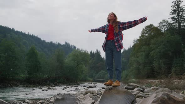 Happy Female Hiker Standing at Rocky River Shore