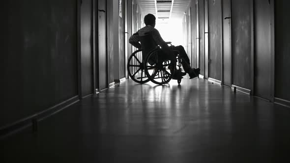 Disabled Man Riding Wheelchair along Hallway