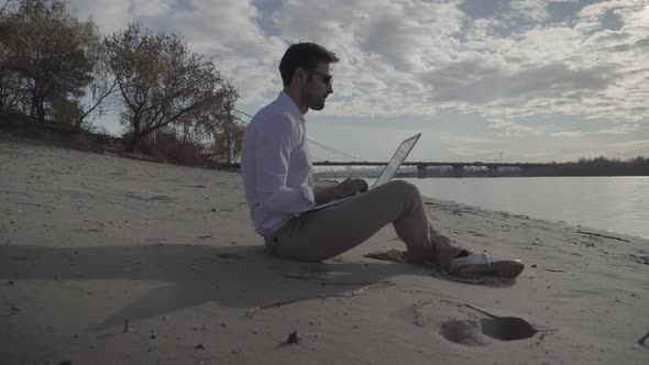 Man Freelancer Using Laptop Online Social Network In Internet. Man Sitting On Beach And Working.