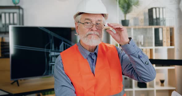 Construction Worker in Helmet and Vest which Taking off His Glasses while Looking Into Camera