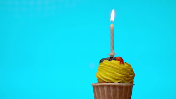 Delicious Festive Cupcake with Yellow Cream with a Burning Candle Spinning on a Light Blue