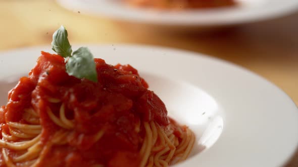 Camera follows grinding pepper over fresh tomato sauce spaghetti in plate. Slow Motion.