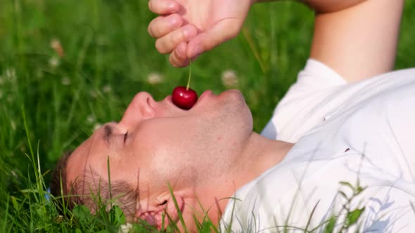 Man Relaxing Lying on the Grass in the Garden and Eating Juicy Ripe Cherries