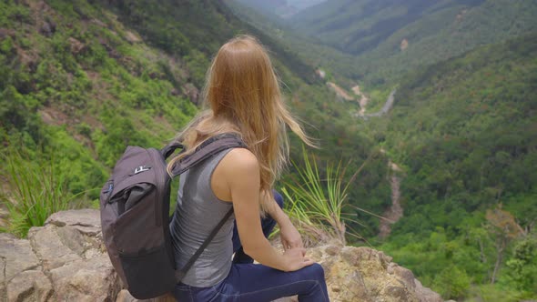 Young Woman-traveler with a Backpack in the Mountains. She Is Looking at the Majestic Valley Down