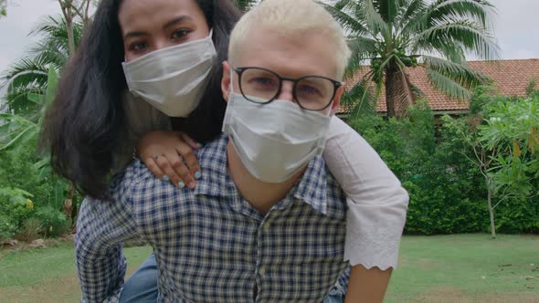 Young Mixed Race Couple Wearing Protective Mask Running Piggyback and Having Fun at the Home Garden