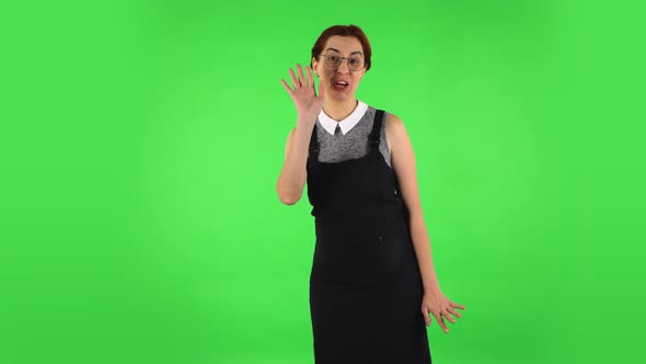 Funny Girl in Round Glasses Is Waving Hand Hello, Flirting. Green Screen