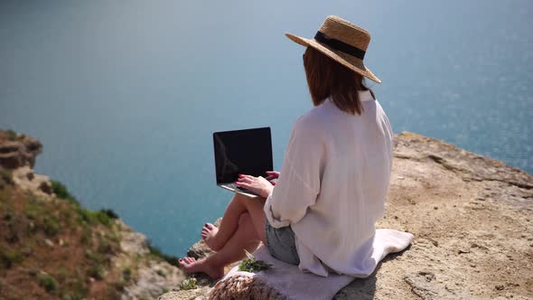 Successful Business Woman in Yellow Hat Working on Laptop By the Sea