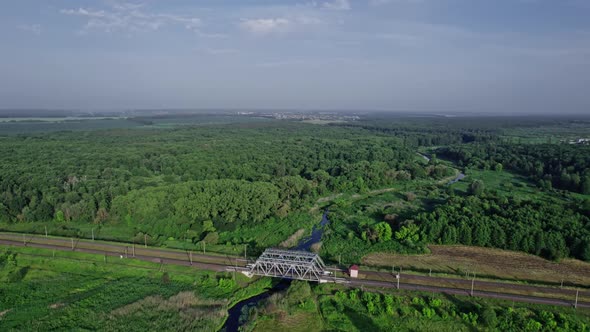 Small River Flows Smoothly Between Green Fields and a Railway Bridge