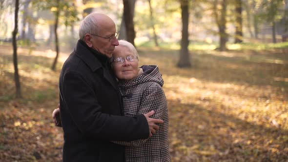 Loving Elderly Couple Cuddling Among Autumn Park