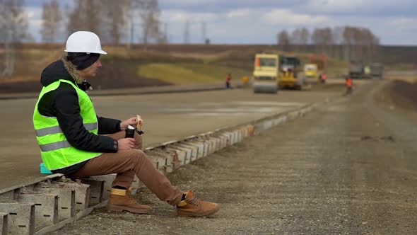 Engineer Sitting on the Road, Eating a Sandwich. Lunch Break