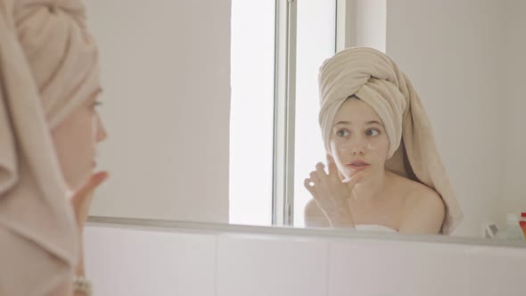 Teenage girl looking at the mirror in the bathroom - checking her face