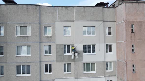 An Industrial Climber Suspended on Ropes and Paints the Wall of a Building with a Roller