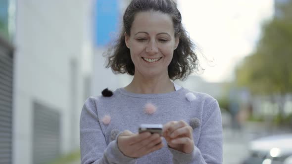 Front View of Smiling Middle Aged Woman Using Smartphone.