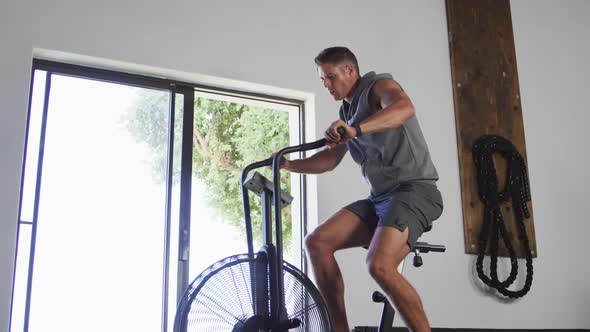 Fit sweaty caucasian man exercising on training bike inside gym