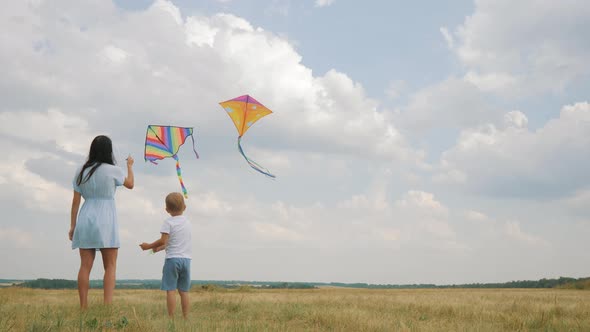 Happy Family Mom and Son Playing with Flying Kite on Meadow in Beautiful Sunny Day Blue Sky