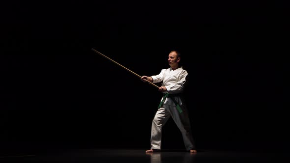 Kendo Fighter on White Kimono Practicing Martial Art with the Bamboo Bokken on Black Background.